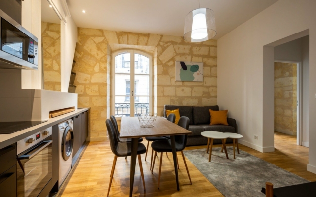 Sainte Catherine Salle à manger avec grande table, espace avec canapé, décoration mur en pierres.