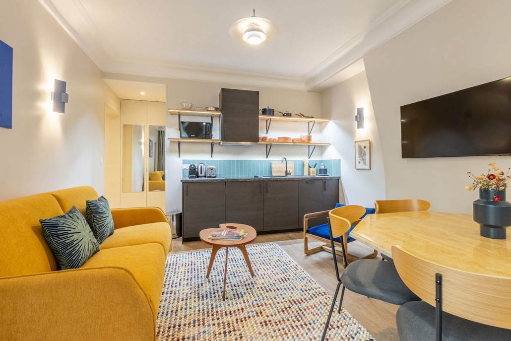 Vue panoramique de la suite urbaine avec cuisine équipée, canapé, table à manger et TV.