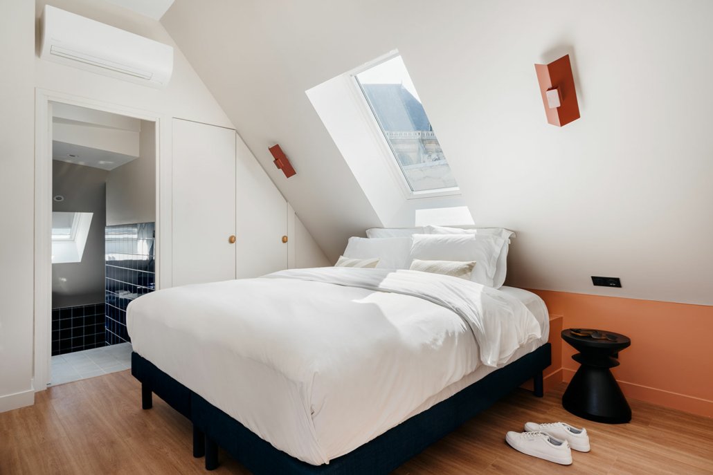 Chambre avec lit double, décorée de façon épurée dans des tons blanc et saumon.