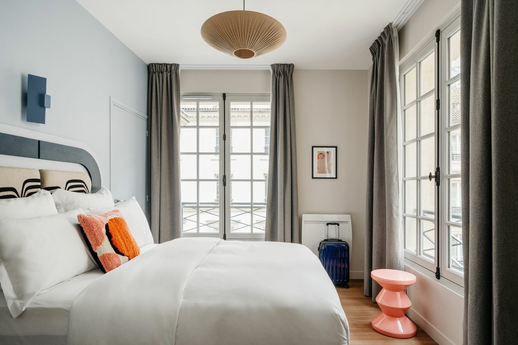 Chambre avec lit double et deux fenêtres, décorée dans des tons chauds.