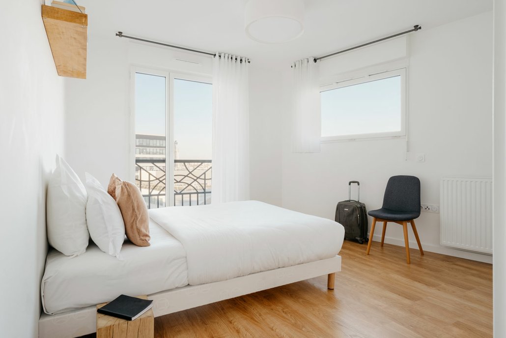 Chambre avec lit simple et porte fenêtre. Décorée dans des tons blancs.