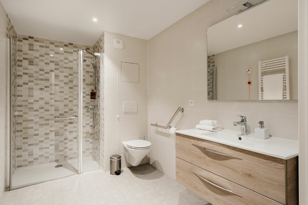 Salle de bain entièrement équipée, avec douche à l'italienne. Couleur beige.